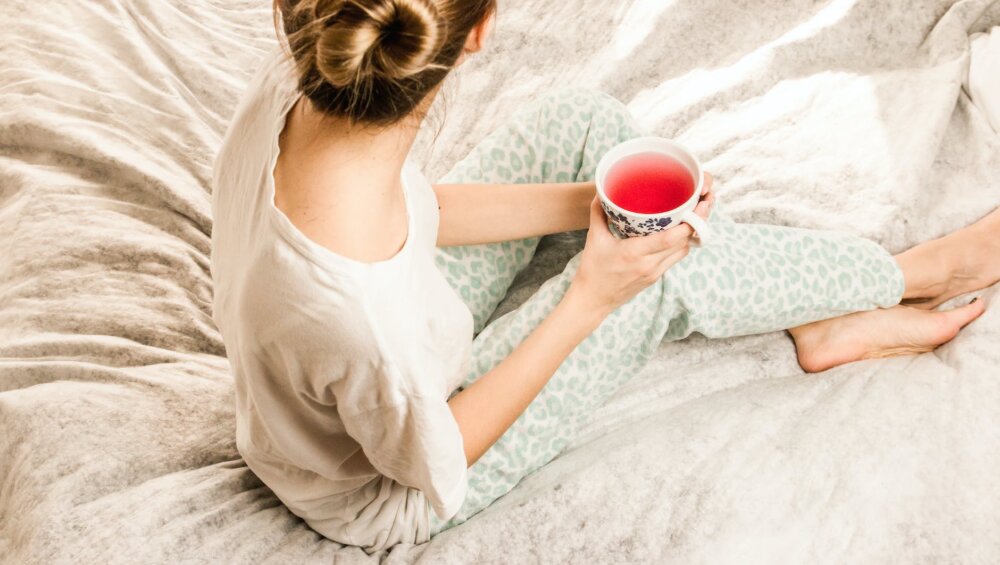 aerial view photography of woman sitting on blanket while holding mug filled with pink liquid looking sideward