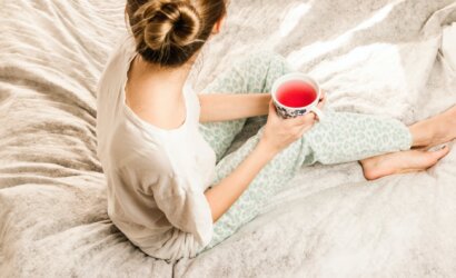 aerial view photography of woman sitting on blanket while holding mug filled with pink liquid looking sideward