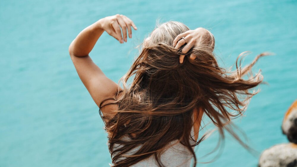back view photo of woman in white sleeveless shirt running her fingers through her hair