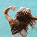 back view photo of woman in white sleeveless shirt running her fingers through her hair