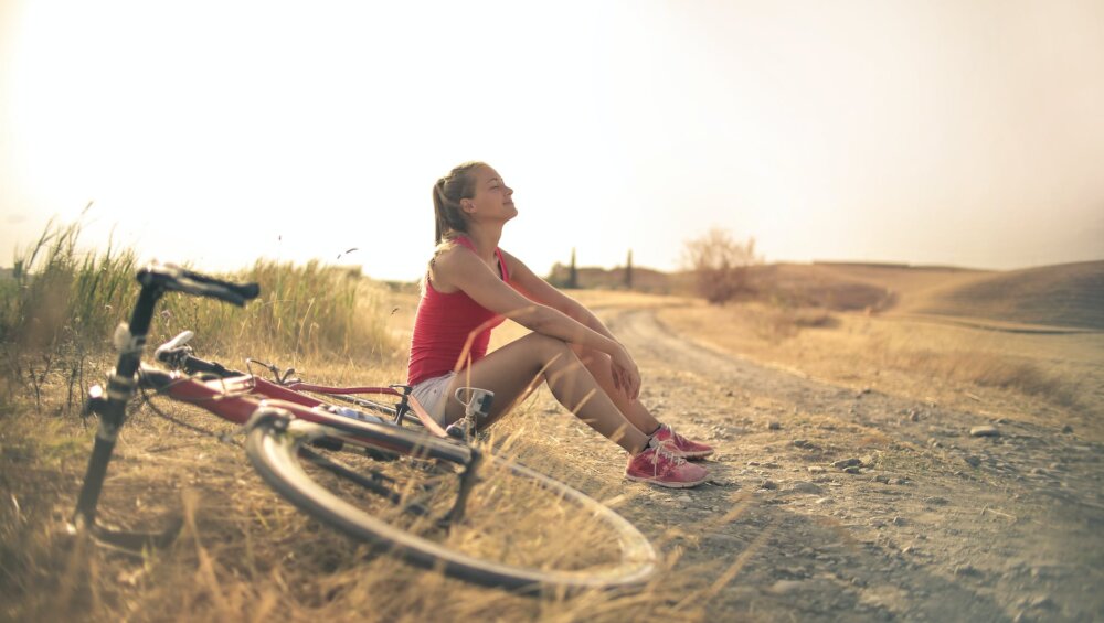 sportive woman with bicycle resting on countryside road in sunlight