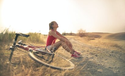 sportive woman with bicycle resting on countryside road in sunlight