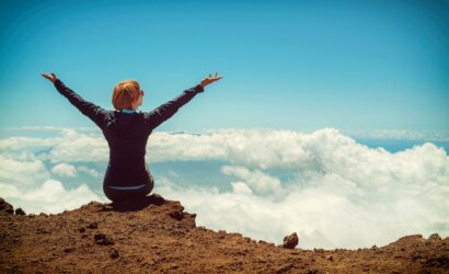 person sitting on cliff raising up both hands