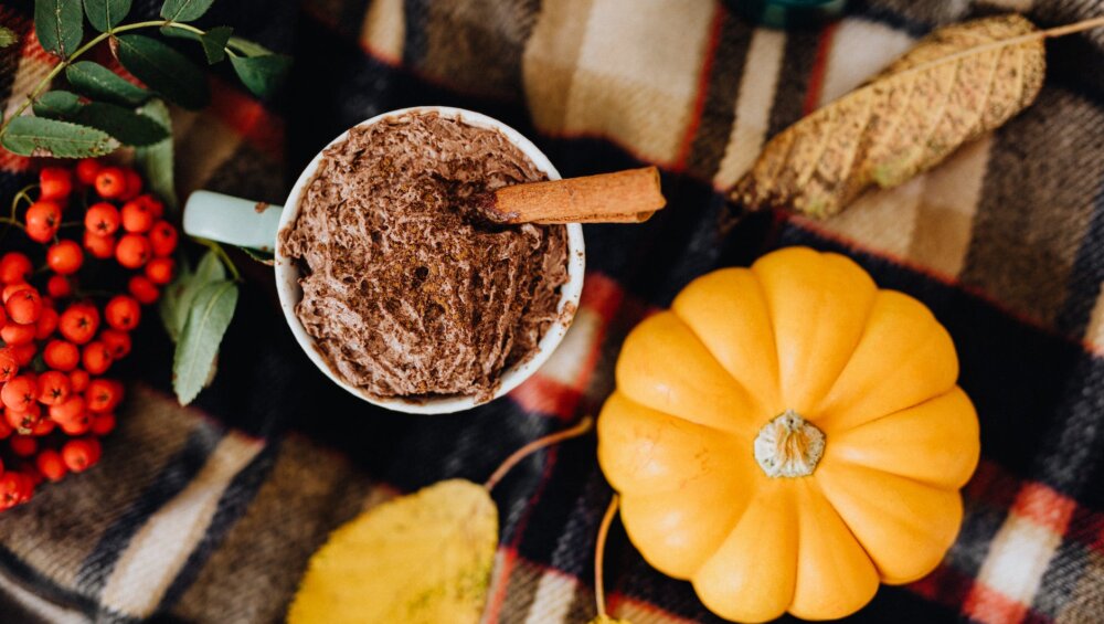 cinnamon stick on a chocolate drink beside pumpkin